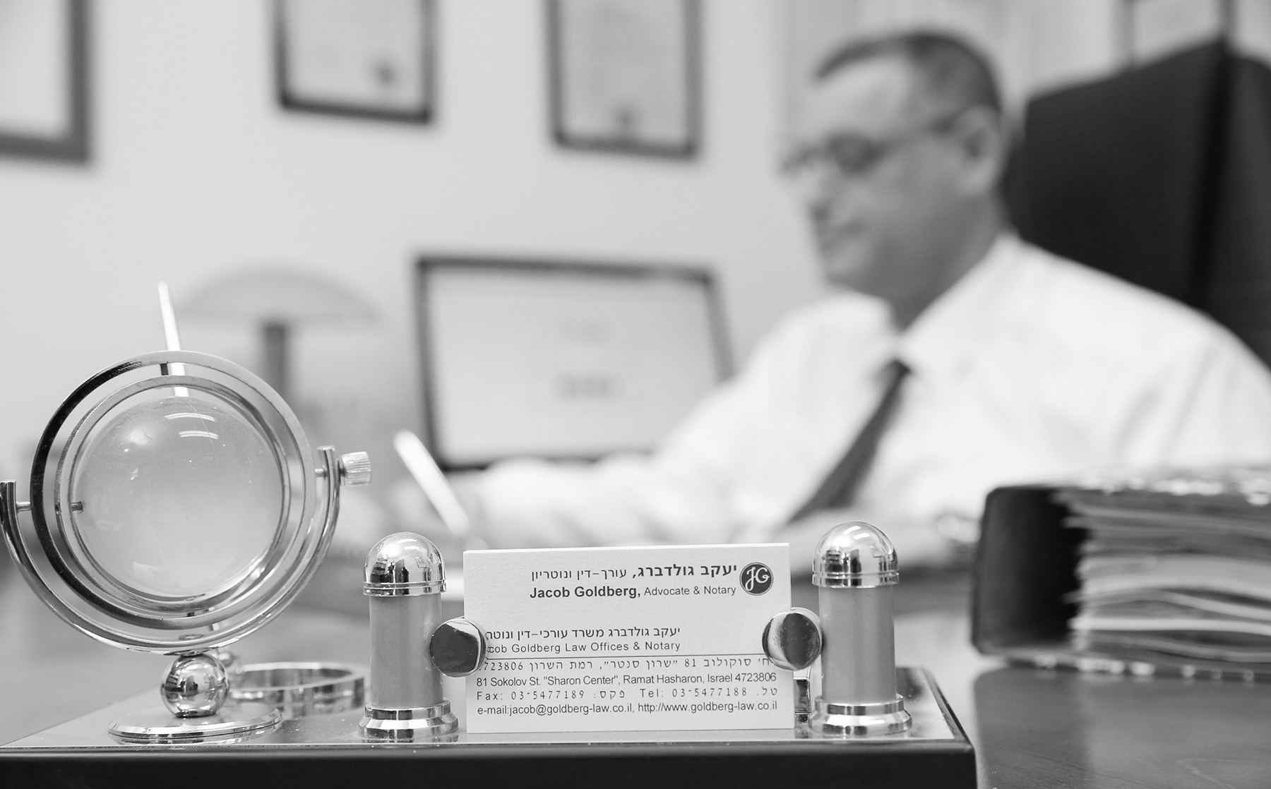 כרטיס הביקור של עו״ד יעקב גולדברג על שולחנו, והוא חותם על מסמך ברקע